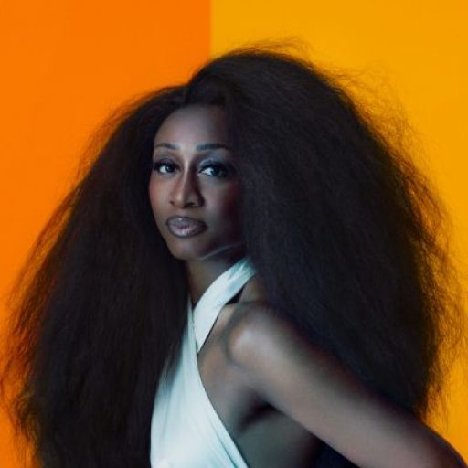 Beverley Knight in front of an orange background wearing a white halterneck top